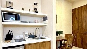 Une cuisine compacte équipée d’un four à micro-ondes, d’une machine à café et d’un évier. On y trouve un meuble en bois sous le plan de travail, ainsi qu’une table à manger avec des chaises.