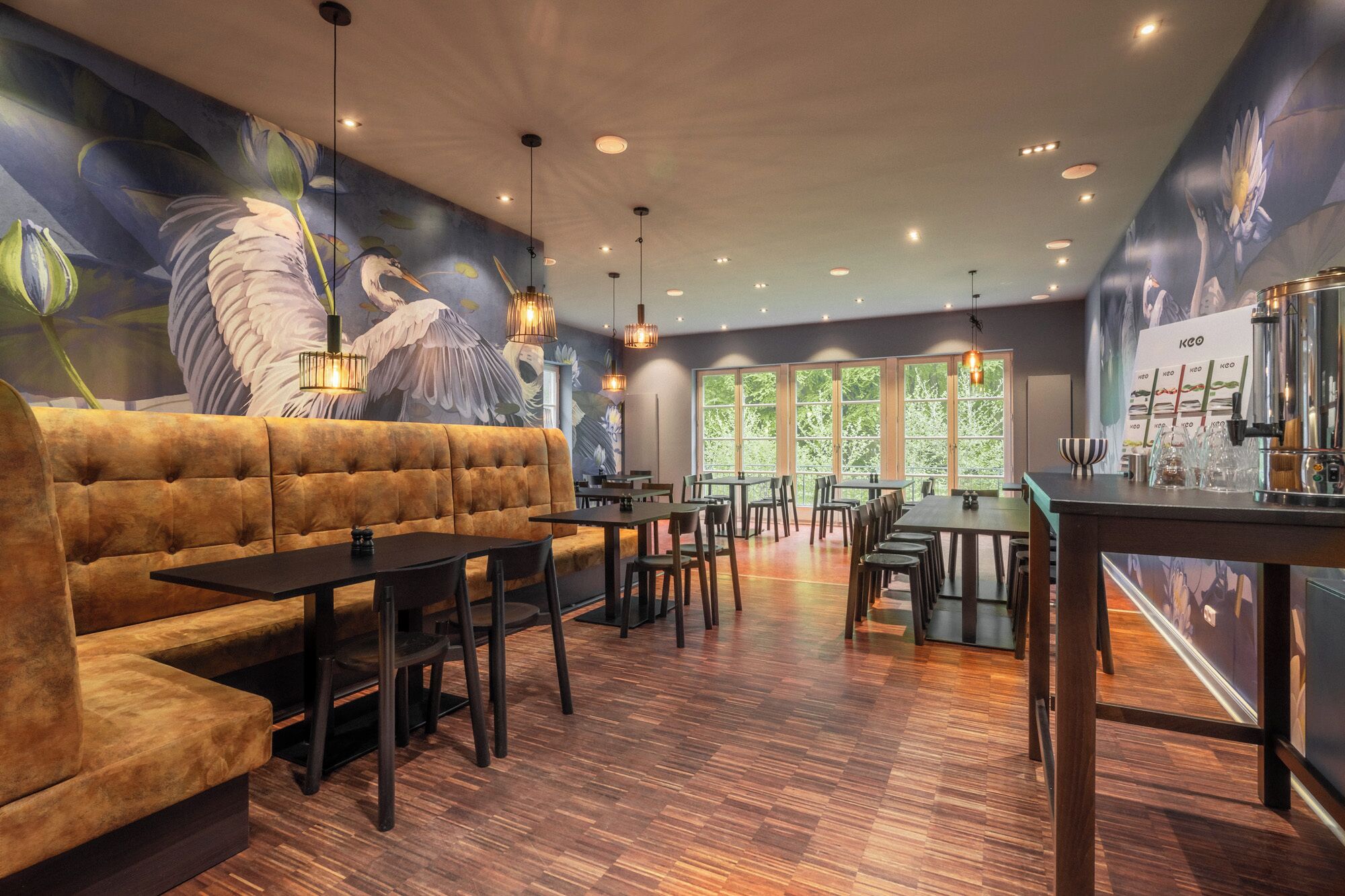 Interior de un restaurante con un mural, asientos acolchados, mesas de madera y una zona de bar.