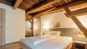 Un dormitorio con techo de madera, una cama con ropa de cama blanca, una mesita de noche y un buró con una lámpara.