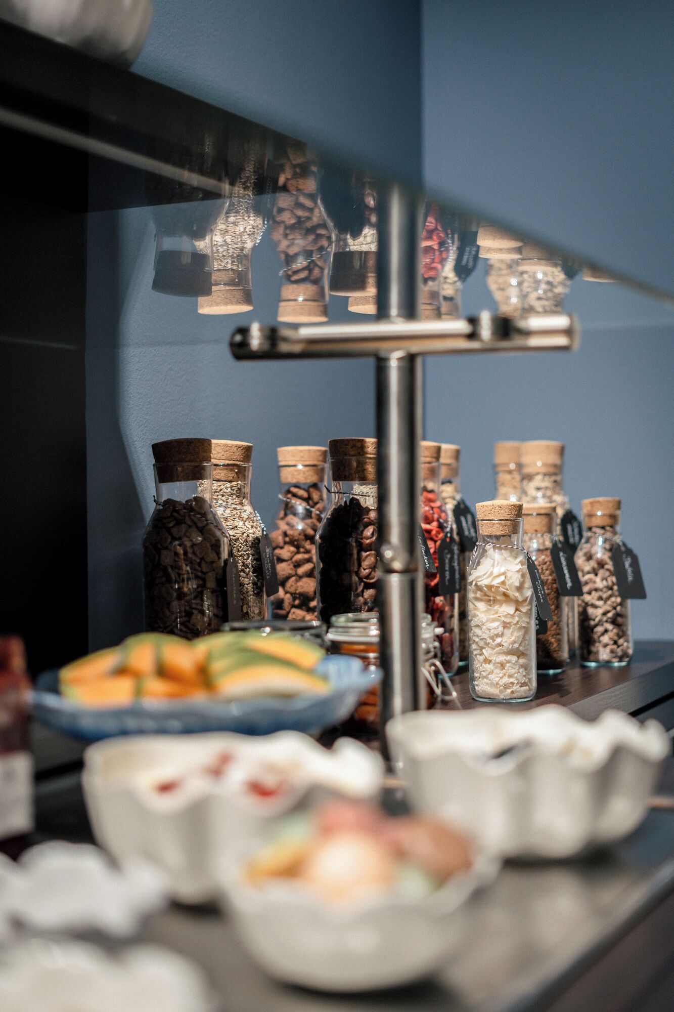 En udstilling af forskellige fødevarer og krydderier i glasbeholdere med korkpropper, arrangeret på en hylde.