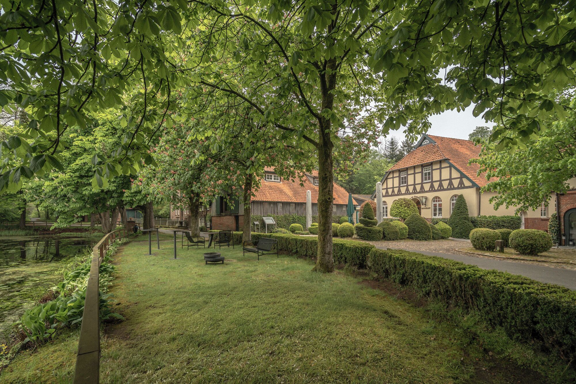 Ein traditionelles Gebäude im europäischen Stil mit einem Ziegeldach, umgeben von gepflegten Hecken und einer Rasenfläche mit Bänken.