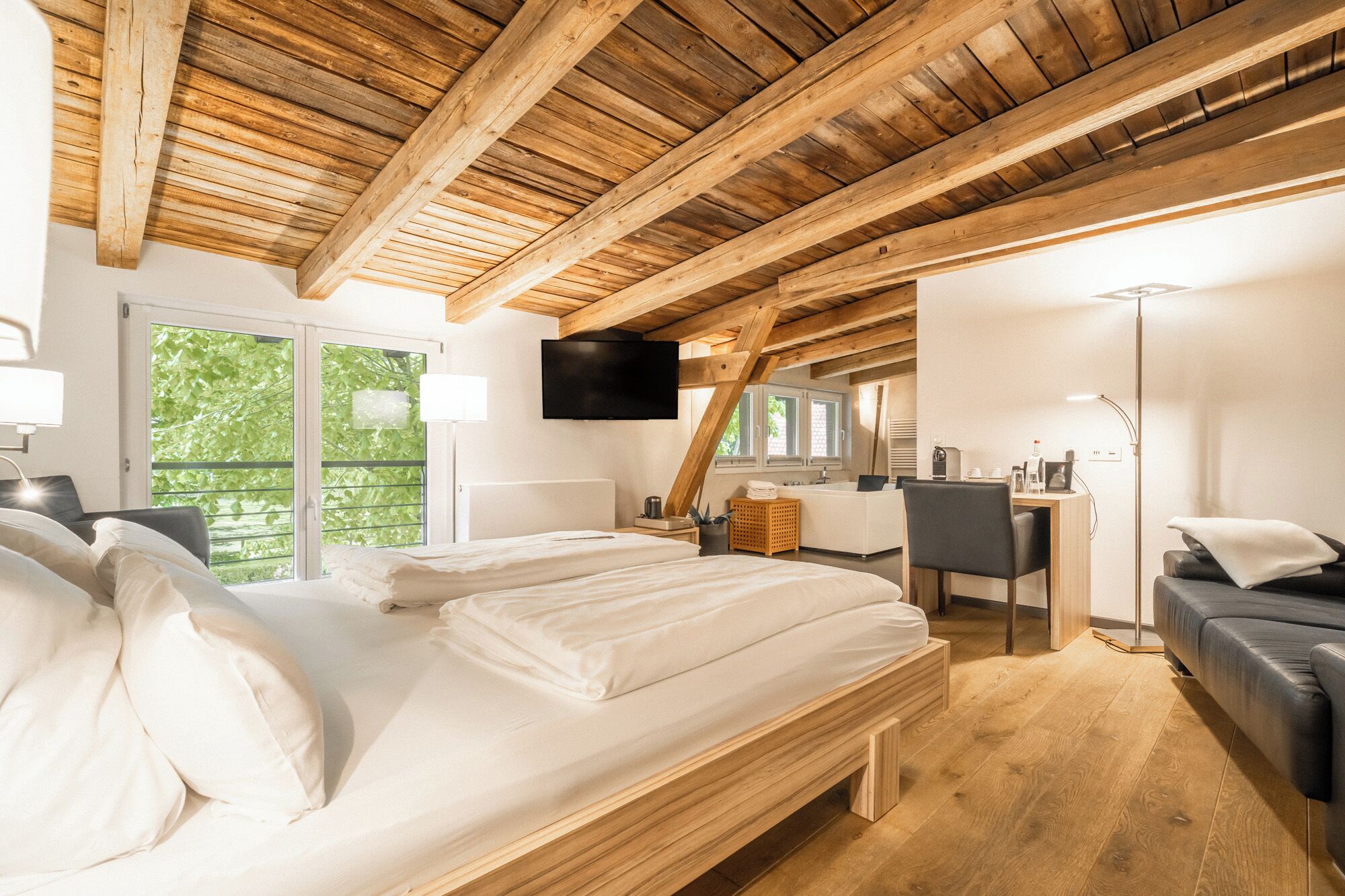 Quarto com teto de madeira, uma cama, escrivaninha, cadeira e televisão.