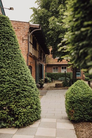 A brick building with a covered walkway, surrounded by well-maintained hedges. - Klostermühle (Groß Meckelsen)