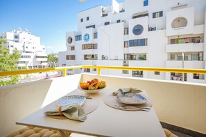 Ein Balkon mit Tisch für zwei Personen, einer Obstschale und Blick auf weiße Häuser.