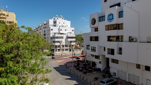A multi-story building with balconies, a street with a pedestrian crossing, and outdoor seating areas.