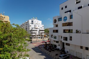 Ein mehrstöckiges Gebäude mit Balkonen, eine Straße mit Fußgängerüberweg und Außenbereichen mit Sitzgelegenheiten.