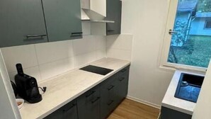A compact kitchen with grey cabinets, a white countertop, and a window with a view of greenery. - Vacation village Seddiner See - Bungalow 2 (Seddiner See)