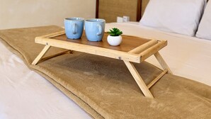 Een bed met een houten dienblad waarop twee kopjes en een kleine plant staan.