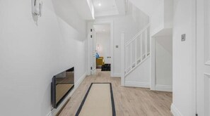 A modern hallway with a flat-screen TV, a wooden floor, and a staircase. - Modern Luxury Apartment in Jewellery Quarter – Central Birmingham Stay (Birmingham)