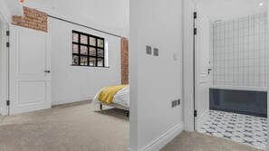 A bedroom with a bed, a window, a door, and a bathroom with a tiled floor. - Modern Luxury Apartment in Jewellery Quarter – Central Birmingham Stay (Birmingham)