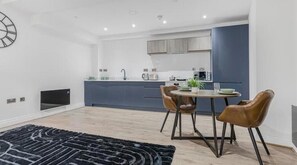 A modern kitchen with a dining area, a clock on the wall, and a flat-screen TV. - Modern Luxury Apartment in Jewellery Quarter – Central Birmingham Stay (Birmingham)