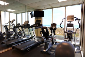 Ein Fitnessstudio mit Laufbändern, Crosstrainern und einem Fernsehbildschirm.