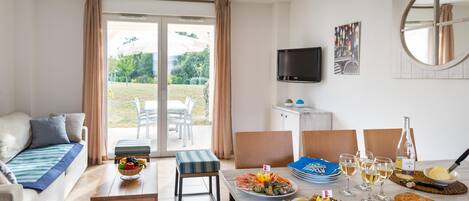 A dining area with a table set for a meal, a sofa, a television, and a view of the outdoors.