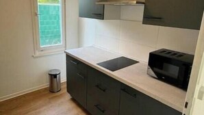 A small kitchen with a window, a microwave, and a trash can.
