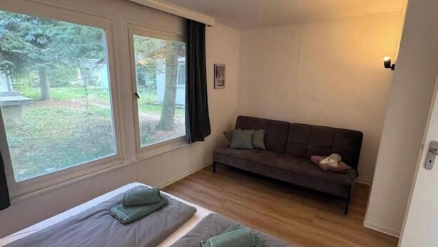 A room with two beds, a sofa, and a window with a view of trees.