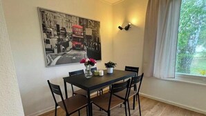 A dining area with a table, chairs, a vase with flowers, a potted plant, and a wall-mounted light fixture.