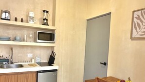 Kompakti keittiö, jossa on pesuallas, mikroaaltouuni, leivänpaahdin ja pieni jääkaappi. Keittiössä on puinen ruokapöytä tuoleineen sekä hedelmäkori.