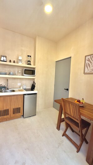 Eine kleine Küche mit Spüle, Mikrowelle, Toaster und einem kleinen Kühlschrank. Ein Holztisch mit Stühlen und einer Obstschale steht bereit.