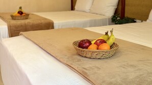 Hotellihuone, jossa on kaksi sänkyä, hedelmäkori sängyllä ja ilmastointilaite seinässä.