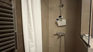 Um chuveiro com um chuveiro manual, uma torneira fixada na parede e um pequeno prateleira com artigos de higiene pessoal.