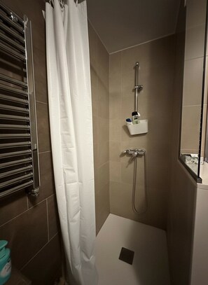 A shower with a handheld showerhead, a wall-mounted faucet, and a small shelf with toiletries. - Apart Sagrada Familia (Barcelona)