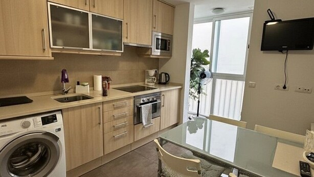 Uma cozinha compacta com máquina de lavar, micro-ondas e uma área de refeições com mesa de vidro e cadeiras.