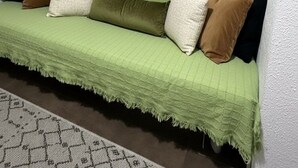 Um sofá verde com várias almofadas, um tapete estampado e um quadro de paisagem na parede.