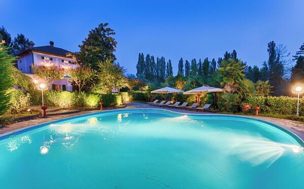 Ein Pool mit Liegestühlen und Sonnenschirmen, umgeben von Bäumen und einem Gebäude.
