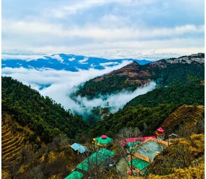 A mountainous landscape with terraced fields, a valley with mist, and a small settlement with colorful buildings. - Four Wooden Rooms ROUTE707 Resorts Orchard Kanatal (Kanatal)