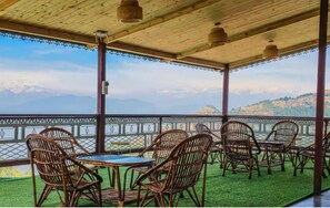 Un espace extérieur abrité, aménagé avec des chaises et des tables en osier, offrant une vue sur un paysage montagneux.