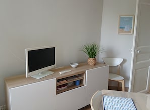 Une pièce moderne et minimaliste, dotée d’un bureau, d’un téléviseur à écran plat, d’un clavier, d’une petite plante et d’un tableau encadré accroché au mur.