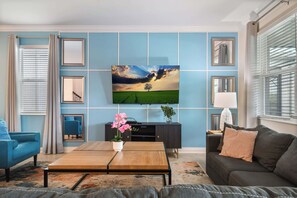 Ein Wohnzimmer mit an der Wand montiertem Fernseher, einer Couch, einem Couchtisch und einem blauen Sessel.