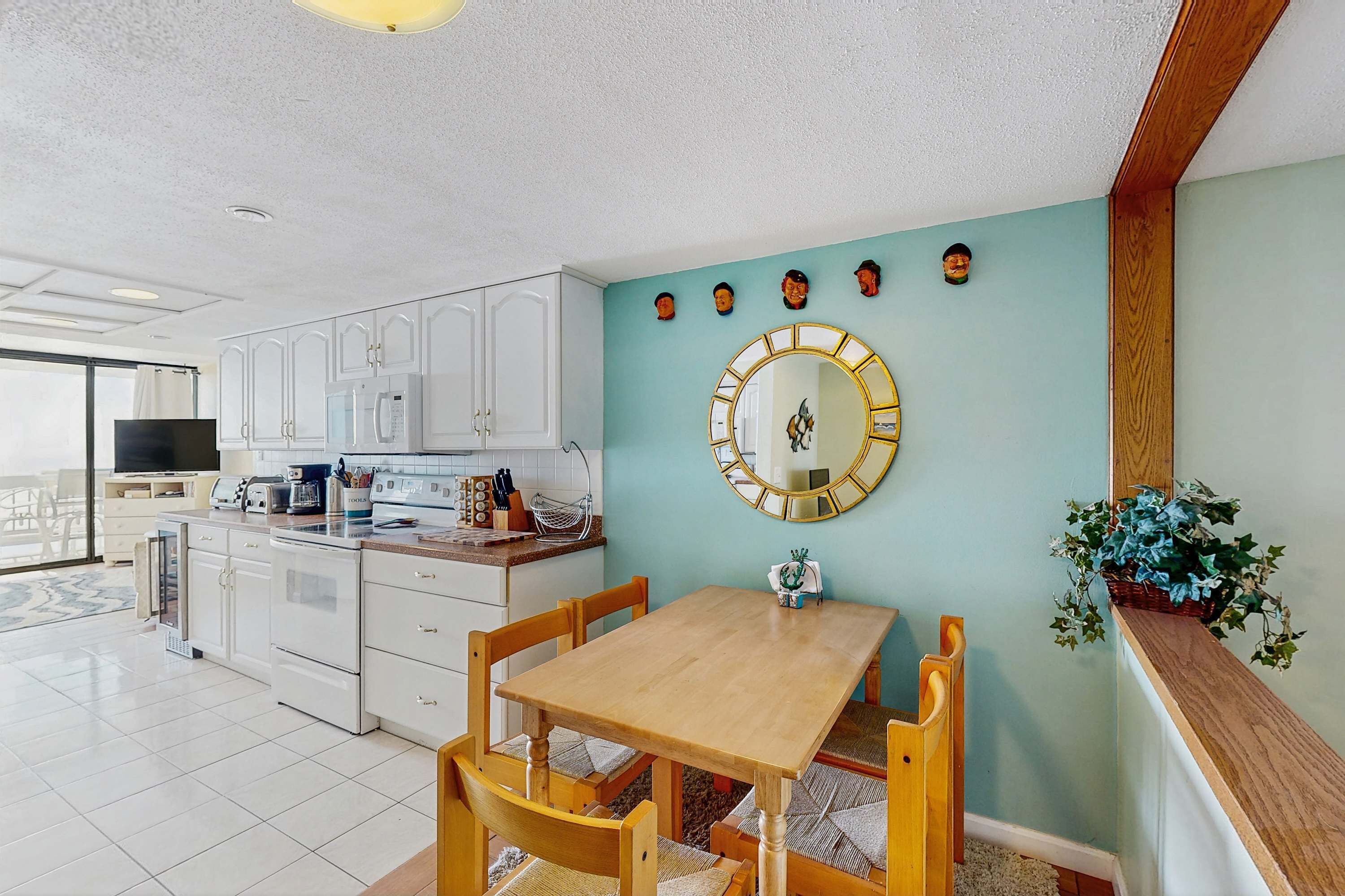 A modern kitchen with white cabinets, a wooden dining table, and a large mirror on the wall.
