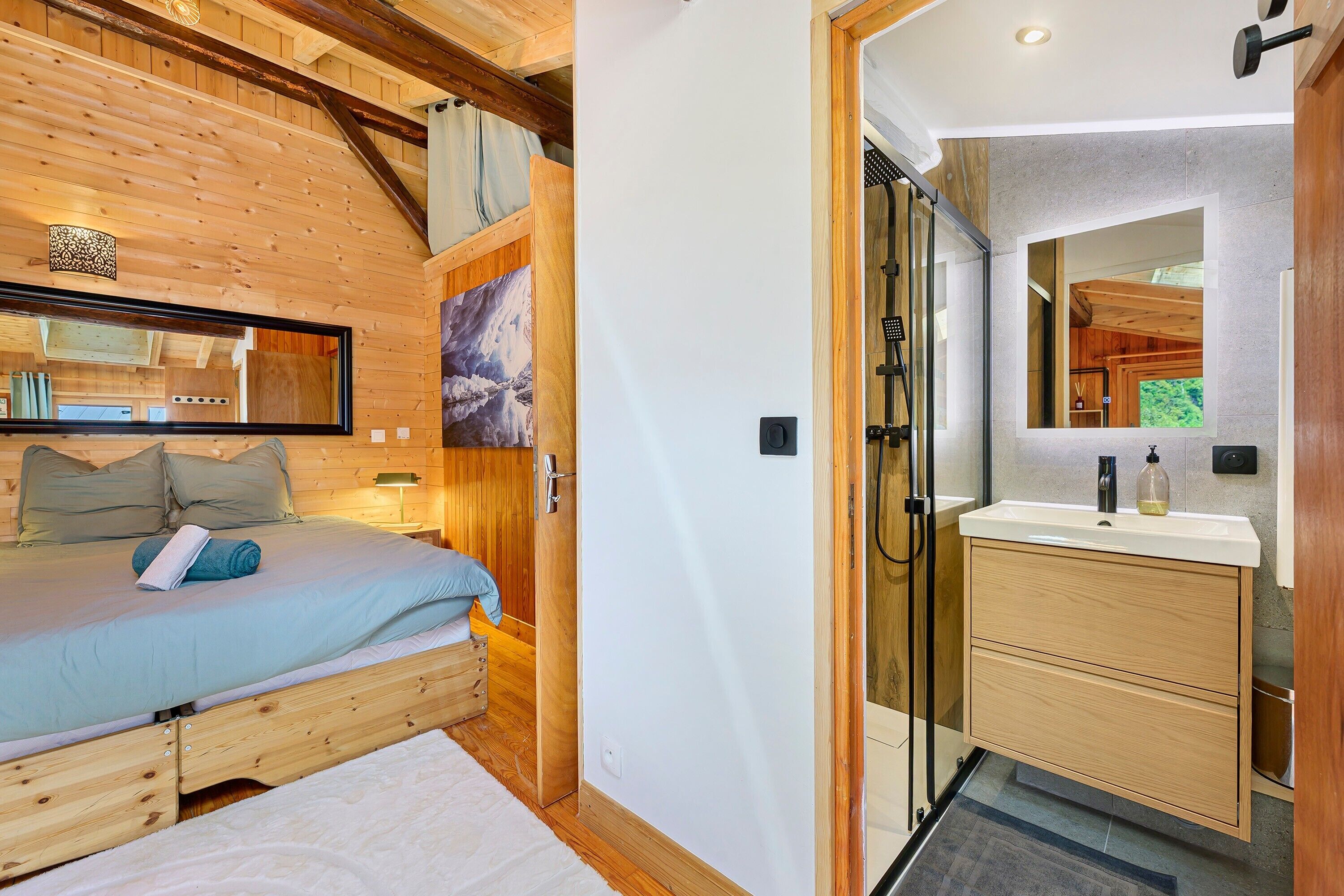 Une chambre à coucher avec un plafond en bois, un lit recouvert d’une couverture bleue, une table de chevet et un grand miroir.