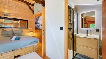 Une chambre à coucher avec un plafond en bois, un lit recouvert d’une couverture bleue, une table de chevet et un grand miroir.
