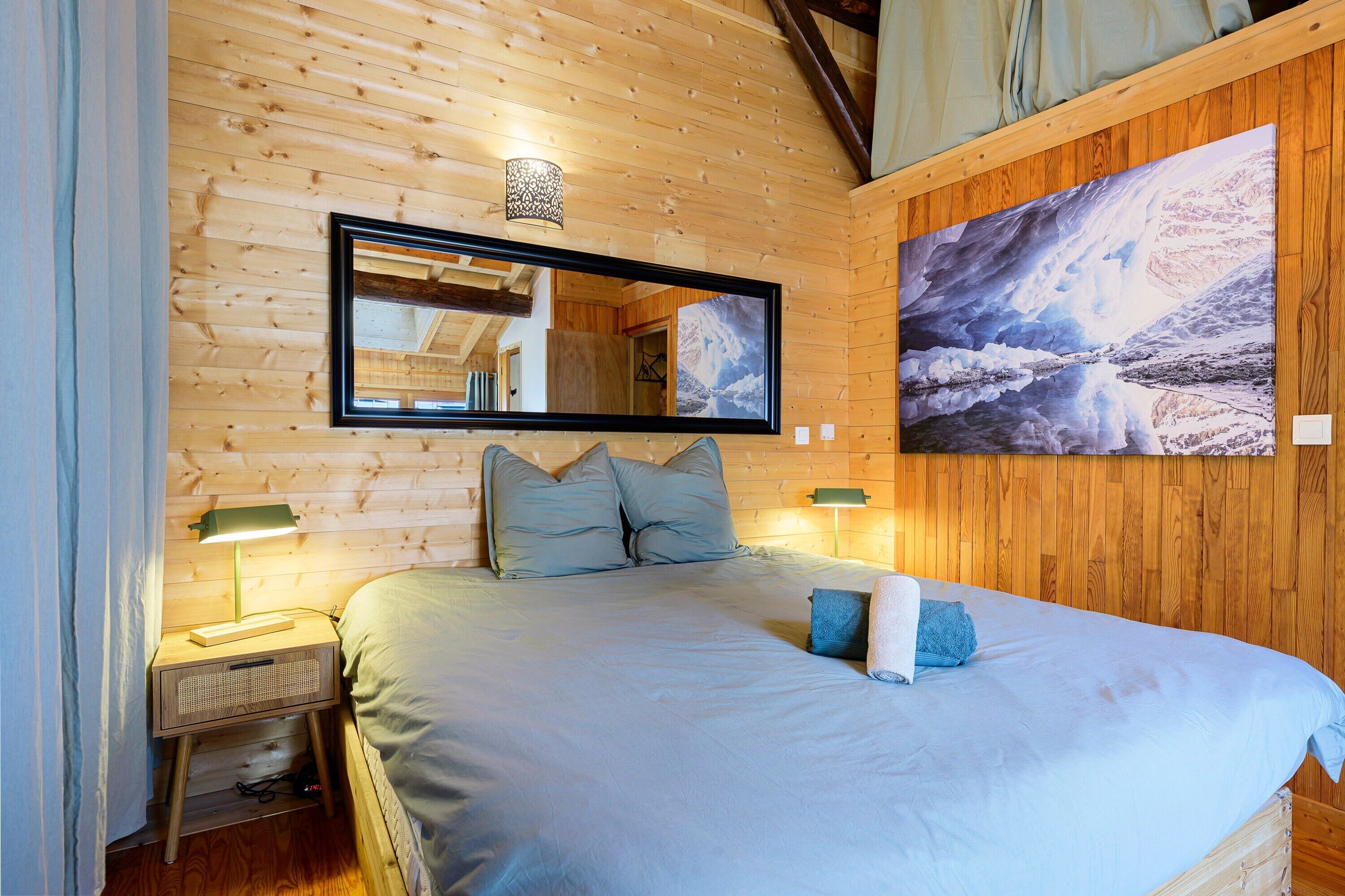 Una stanza con pannelli in legno, un letto, uno specchio, un quadro e un comodino con una lampada.