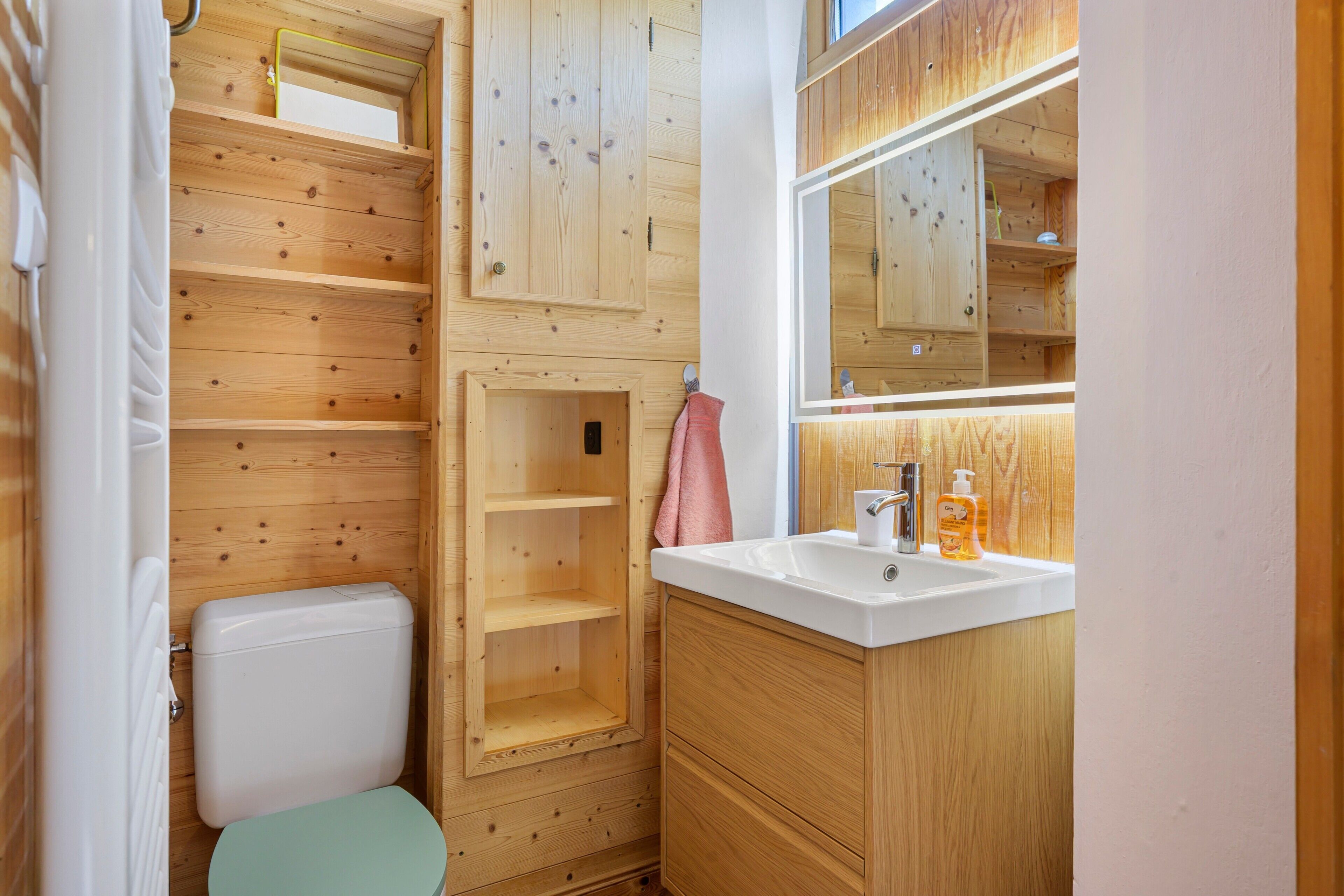 A compact wooden bathroom with a toilet, a sink, and a mirror.