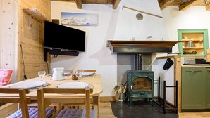 Una habitación acogedora con una mesa de comedor de madera, sillas, un televisor montado en la pared, una chimenea y un armario verde.