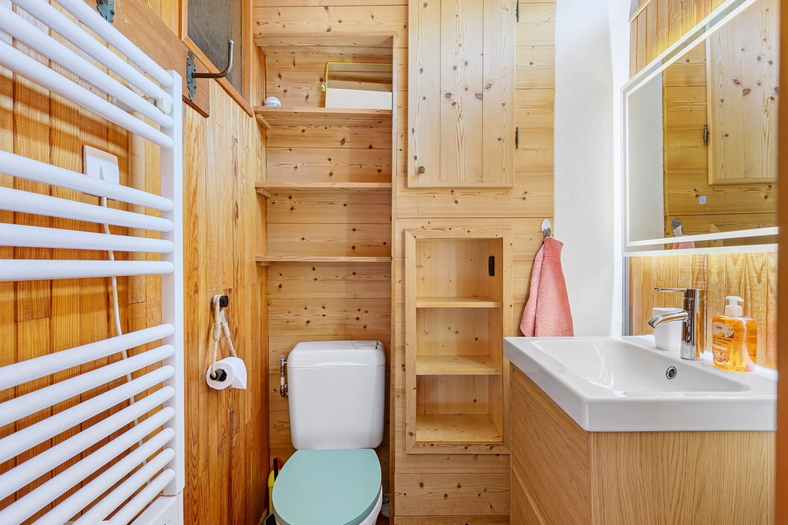 Un baño pequeño de madera con inodoro, lavamanos y estanterías.