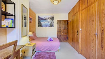A bedroom with a bed, a desk, a chair, a mirror, a painting, and wooden wardrobes.