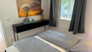 A bedroom with a bed, a nightstand, a painting, and a window with curtains. - Vacation village Seddiner See - Bungalow 4 (Seddiner See)