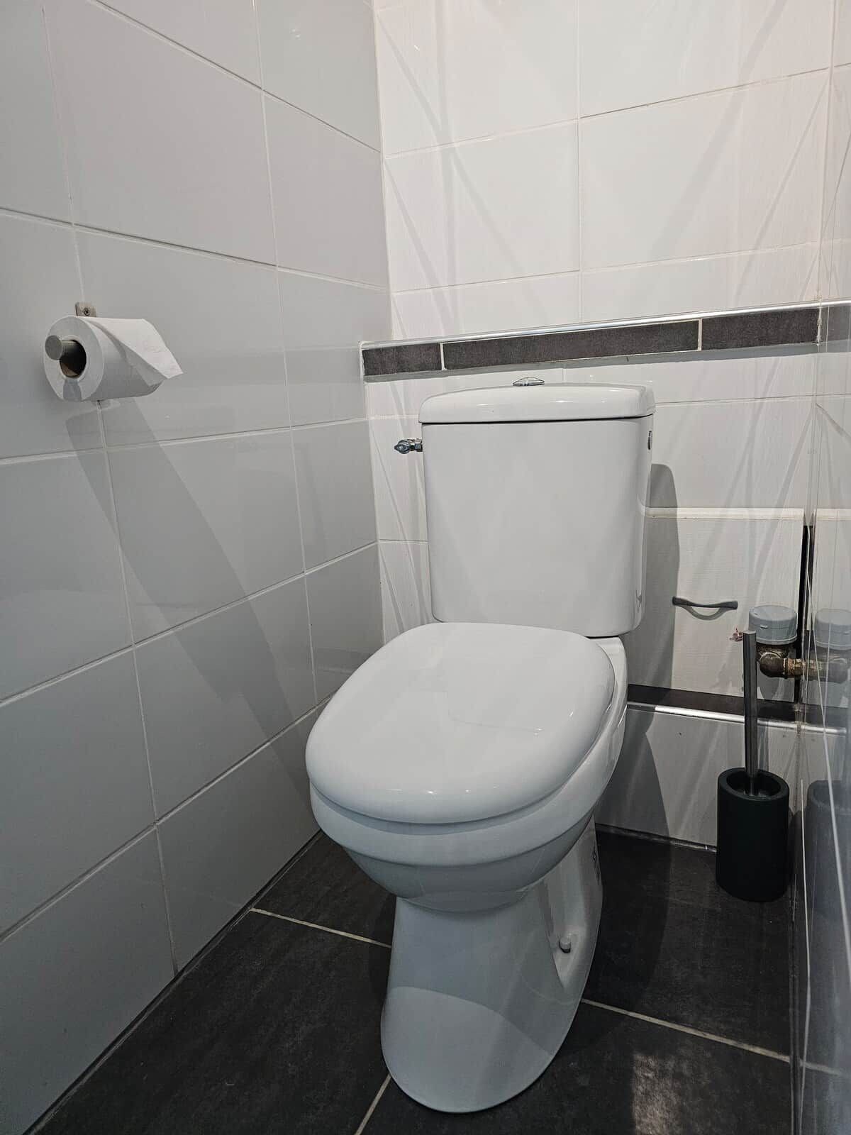 A white toilet with a black base, a toilet paper holder, and a bidet attachment.