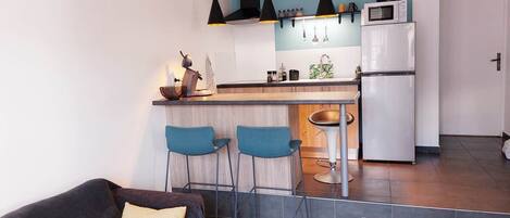 A modern kitchen with a bar area, a dining table, and a sofa in a living area.