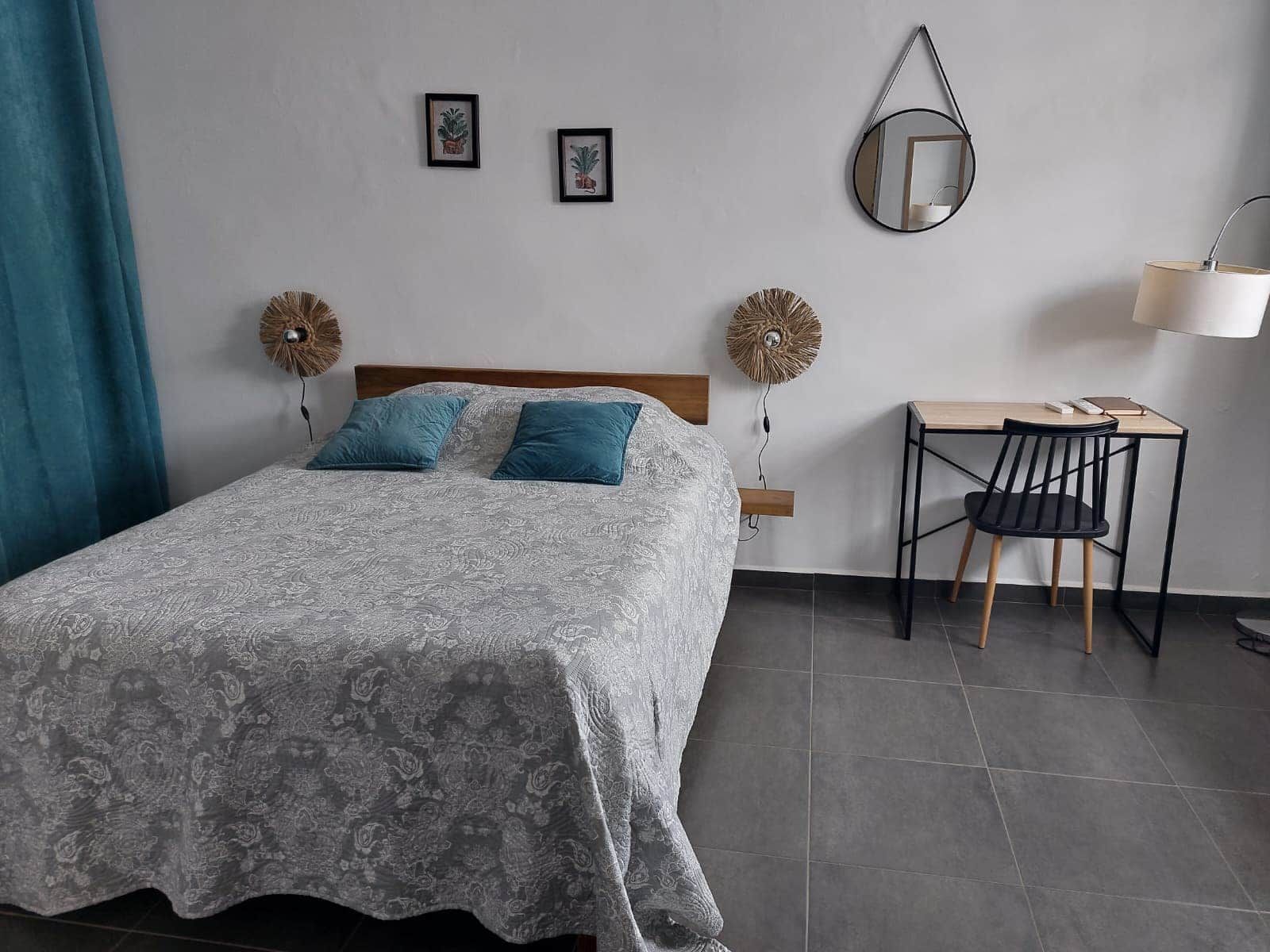 A bedroom with a bed, two pillows, a bedside table with a lamp, a chair, and two wall-mounted decorative items.