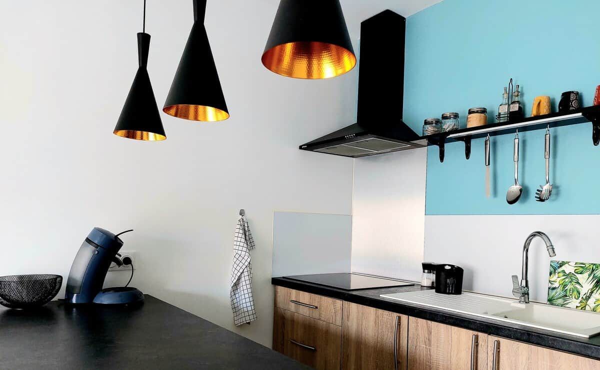 A modern kitchen with pendant lights, a coffee machine, and a hanging utensil rack.