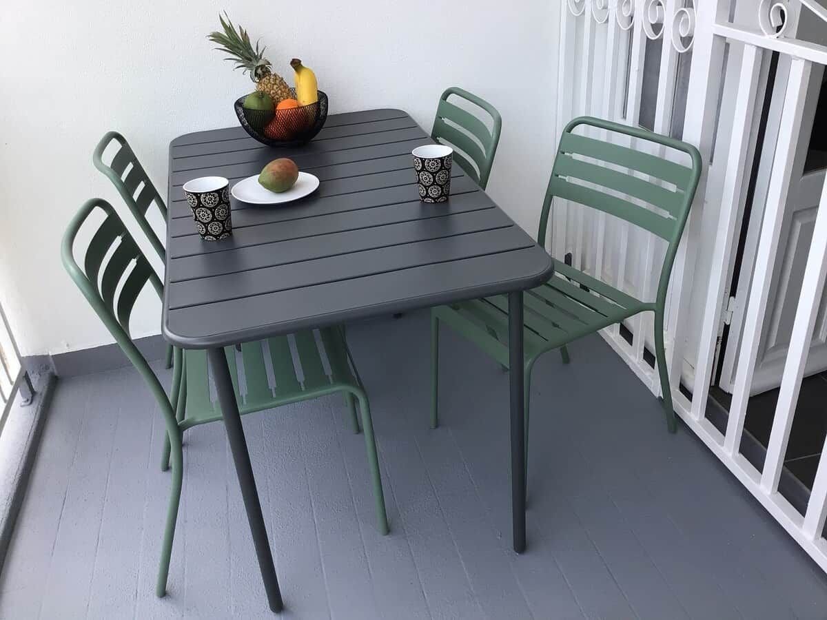Une table avec un panier de fruits et deux tasses, entourée de chaises vertes.