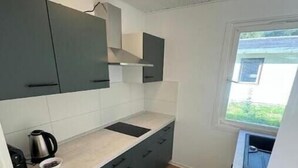A compact kitchen with grey cabinets, a white countertop, and a window providing a view of greenery outside. - Vacation village Seddiner See - Bungalow 5 (Seddiner See)