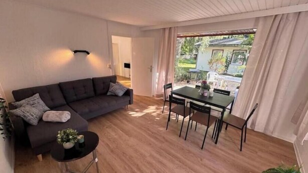 A living room with a sofa, a small round table, and a dining table with chairs. - Vacation village Seddiner See - Bungalow 5 (Seddiner See)