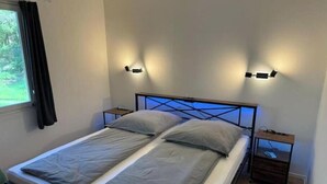 A neatly made bed with a headboard, two bedside tables, and a window with curtains. - Vacation village Seddiner See - Bungalow 5 (Seddiner See)