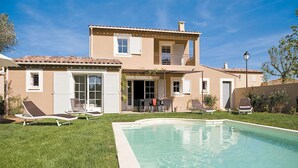 Una casa de dos pisos con piscina, patio cubierto y un pequeño jardín.